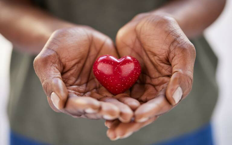 Close up de mãos femininas segurando um pequeno coração vermelho