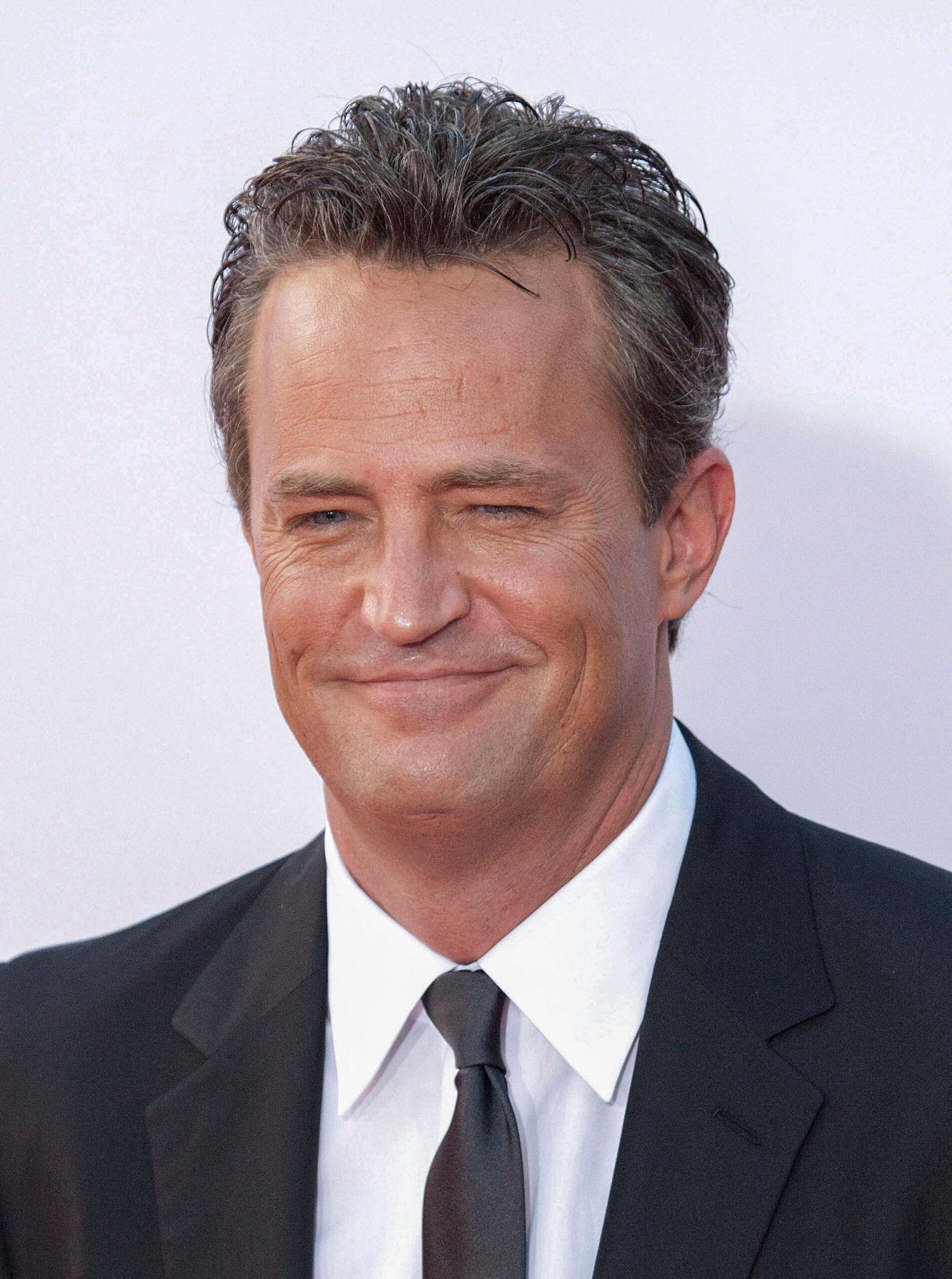 Matthew Perry sorrindo enquanto veste um terno