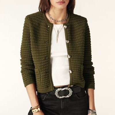 Uma mulher vestindo uma blusa branca e um casaco cardigan verde com calças e cinto pretos