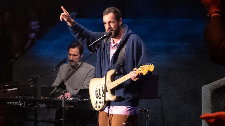 Adam Sandler tocando violão e apontando para cima em Love You