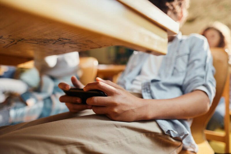 Close up of an unrecognizable student using cell phone under the table during cl