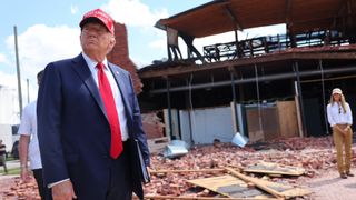 Donald Trump caminha pelos destroços de um furacão usando um chapéu MAGA