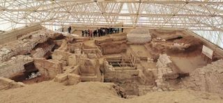 Uma visão ampla das escavações realizadas em Çatalhöyük, mostrando um grupo de pessoas nos limites de uma cidade desenterrada